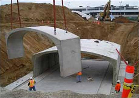 =Construction workers positioning large concrete spans for underground water storage.